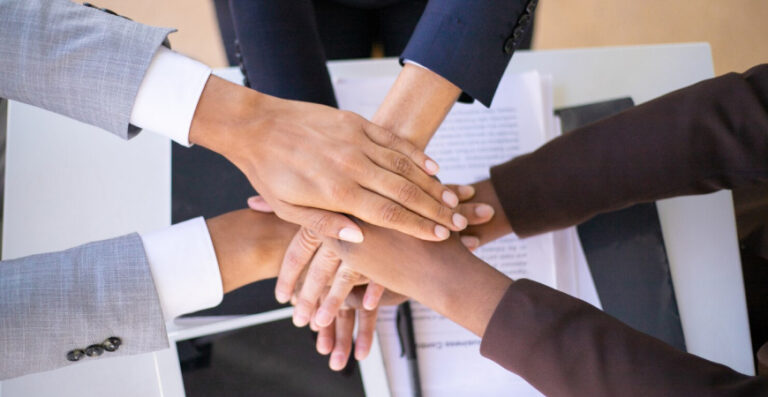 Equipe unindo as mãos em reunião, representando as diferenças entre LTDA e S.A. na organização e governança do negócio.